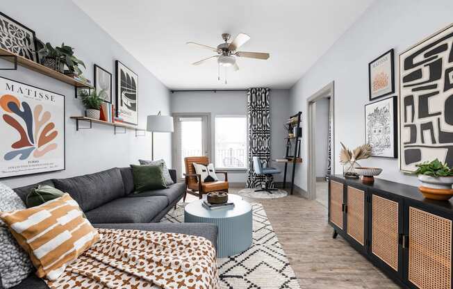 a living room with a gray couch and a blue coffee table and a ceiling fan