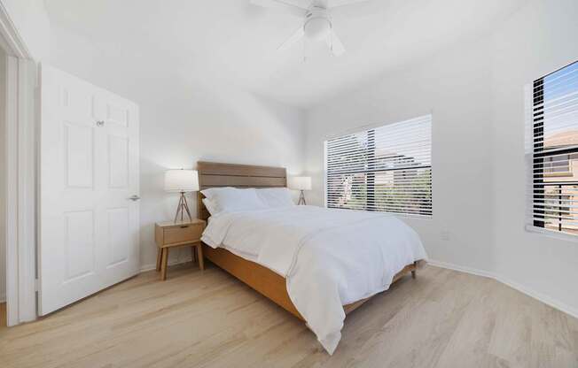 A bedroom with a bed, nightstand, and window with blinds.