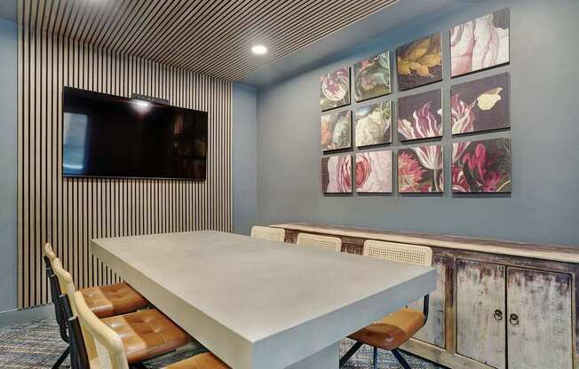 A conference room with a long table and chairs, a television, and a wall of framed pictures.