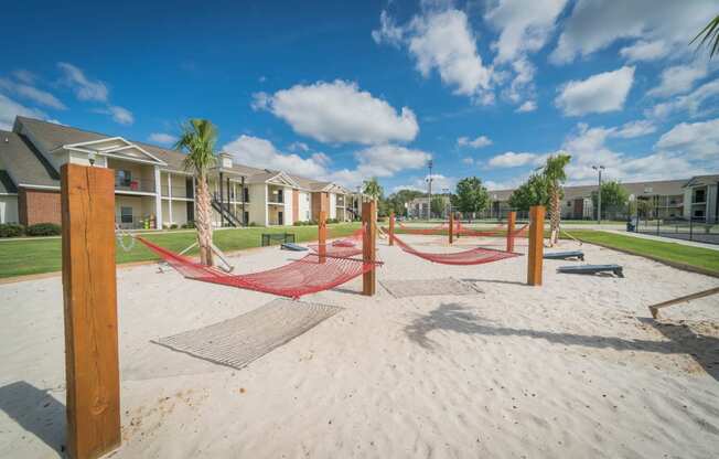 a playground with hammocks on the sand in front of apartment buildings