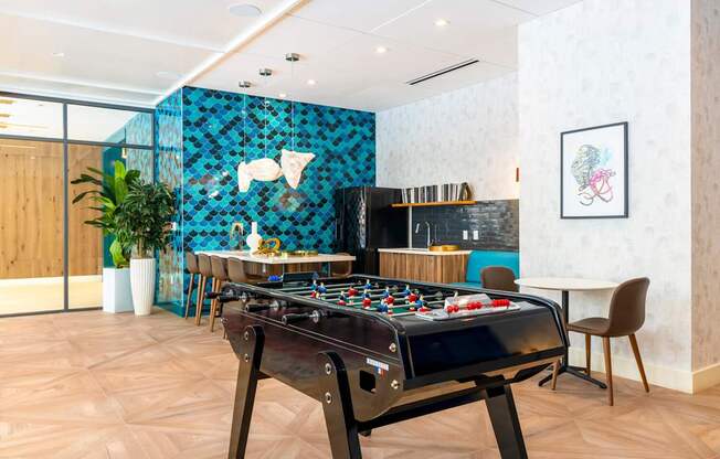 A foosball table is in the middle of a room with a blue tile wall behind it.