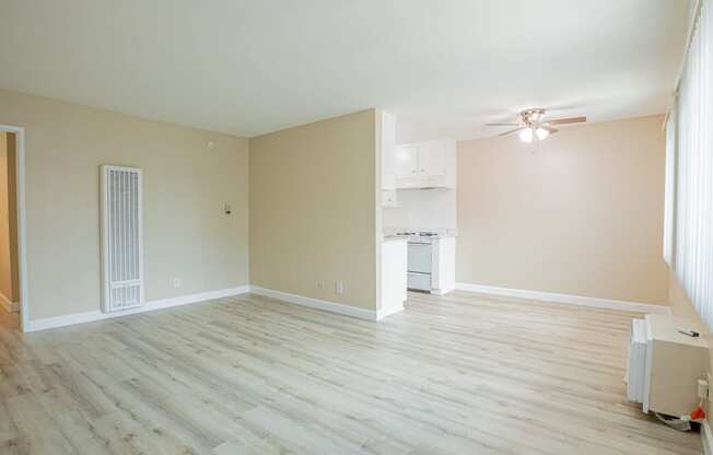 an empty living room with wood floors and a kitchen