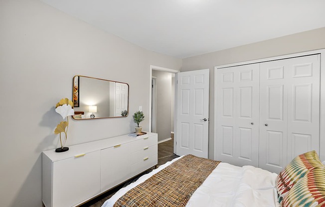 A white bedroom with a bed, dresser, and mirror.