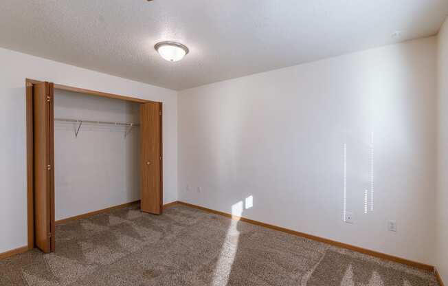 a bedroom area with a closet in a studio apartment.  Fargo, ND Sunwood Apartments  | Living and kitchen Fargo, ND Sunwood Apartments