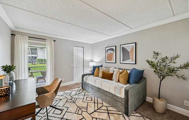 A living room with a grey couch, a wooden table, a rug and a potted plant.