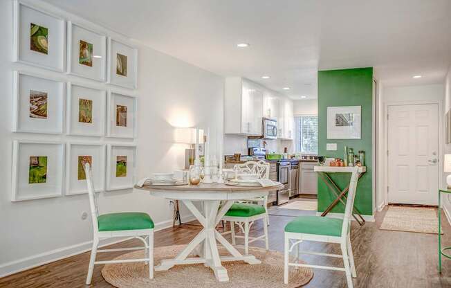 A white dining table with green chairs and pictures on the wall.