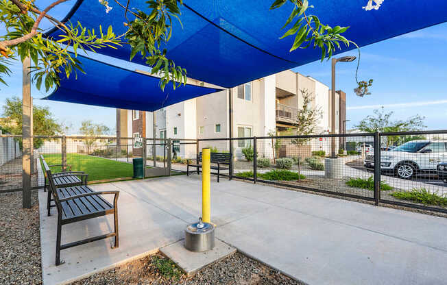 A park bench under a blue canopy with a yellow post in front of it.