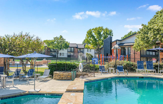 A swimming pool surrounded by lounge chairs and umbrellas with a building in the background.