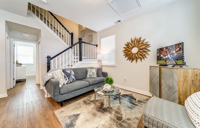 A living room with a grey couch, a glass coffee table, a wooden cabinet, and a wall art.