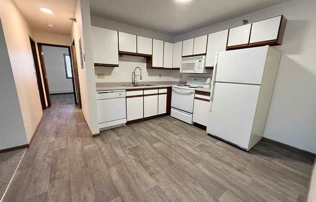 A kitchen with white appliances and wooden flooring.