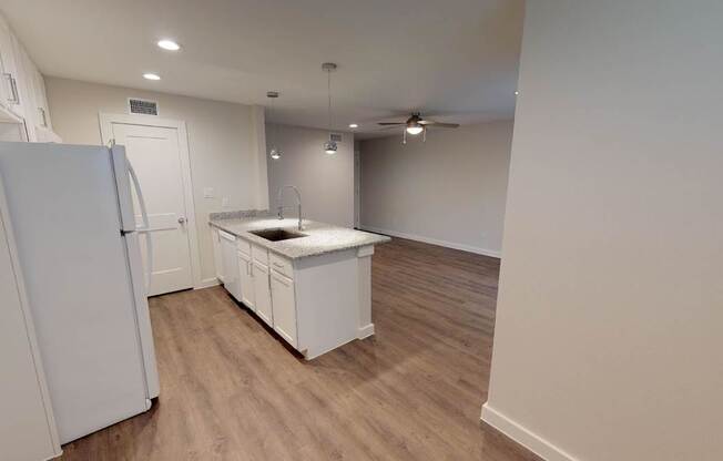 A white refrigerator stands in a kitchen with wooden floors and white walls.