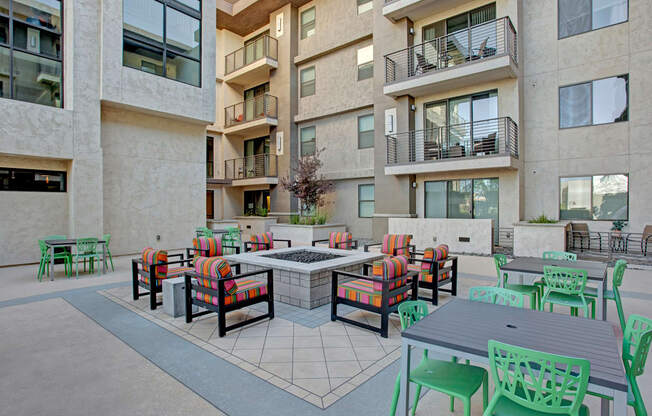 a patio with chairs and tables and a fire pit in front of an apartment building