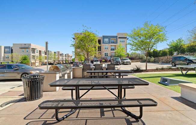 A black picnic table is in the foreground of a sunny day in a parking lot.