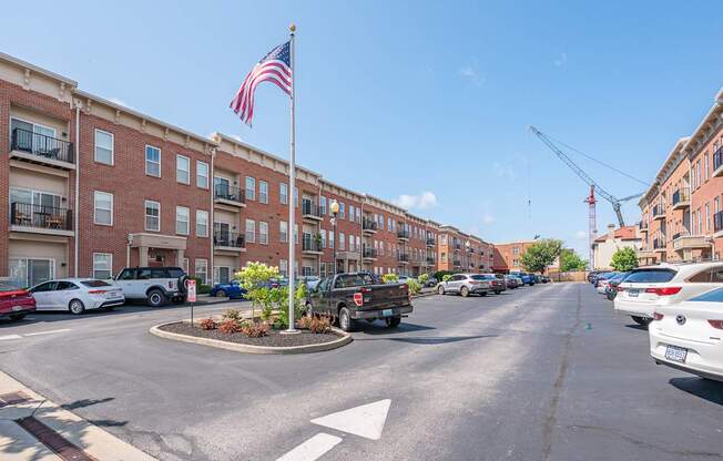 A street view with a flag on a pole and cars parked on the side.