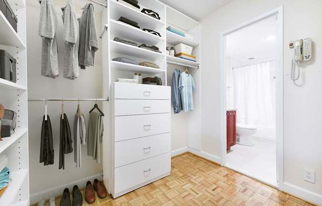 A white closet with clothes hanging and shoes on the floor.