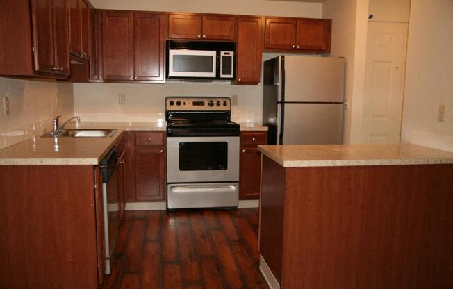 a kitchen with brown wooden cabinets and stainless steel appliances at Heritage Grove Apartments in Renton, WA