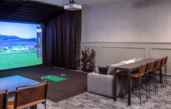 A room with a golf simulator screen and chairs.