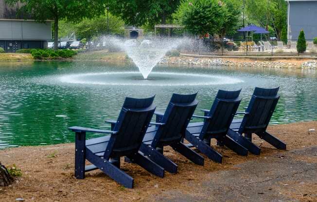 a row of blue adirondack chairs sit in front of a fountain in a pond
