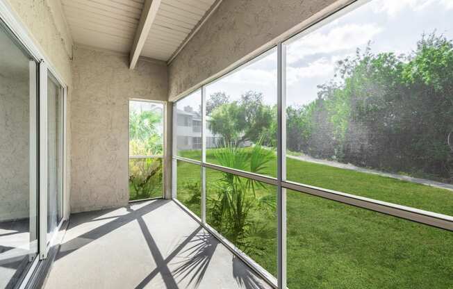 a screened in porch with a view of a grassy area and a building in the background