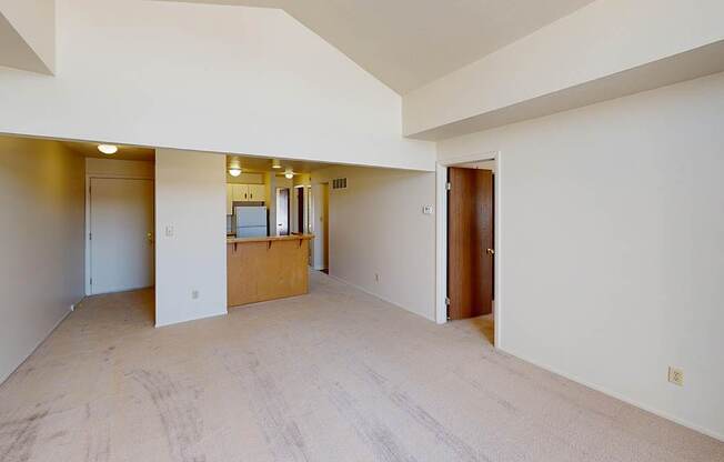 A large empty living room with a high ceiling and a kitchen with a breakfast bar at South Bridge Apartments in Fort Wayne, Indiana
