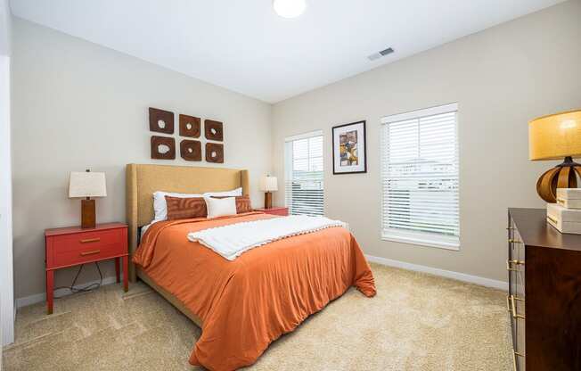 a bedroom with an orange bed and two windows