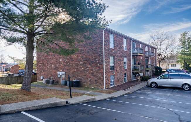 A parking lot in front of a brick building with a tree on the left.