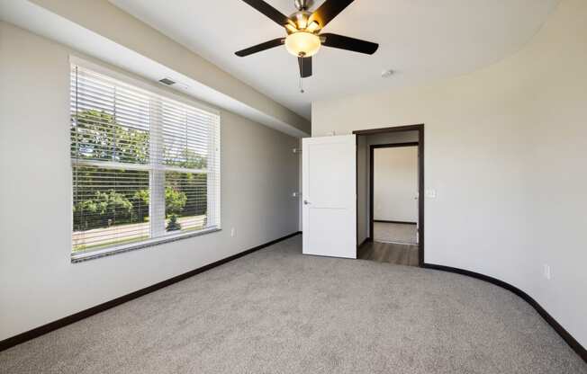 an empty living room with a large window and a ceiling fan