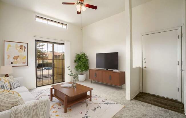 A living room with a white couch, a wooden coffee table, a flat screen TV, and a ceiling fan.
