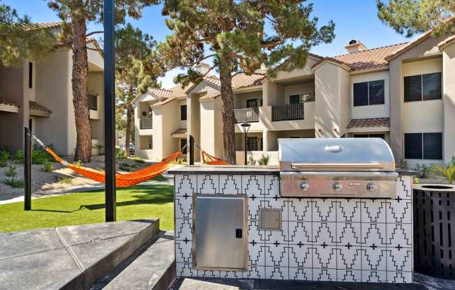 an outdoor barbecue grill with a hammock and apartment buildings in the background