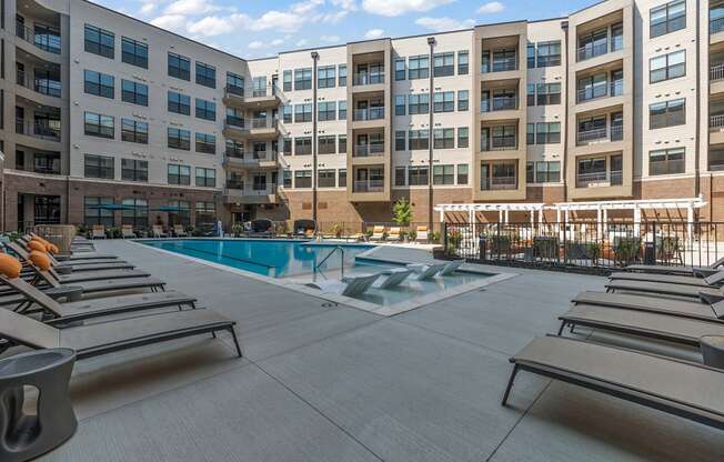an outdoor pool with chaise lounge chairs and a building in the background at The Griffin Royal Oak, Royal Oak, 48067