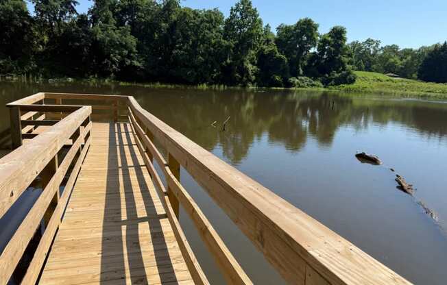 A wooden dock extends into a calm body of water with trees in the background.