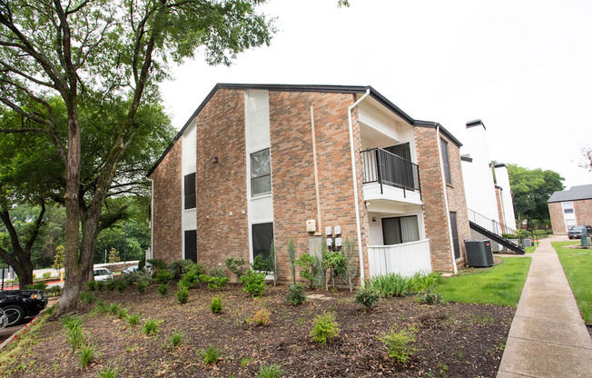 the exterior of an apartment building with a sidewalk and tree