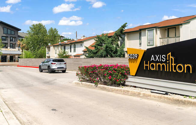 A white car is driving down a street past a building with a sign that says "Axis Hamilton.".