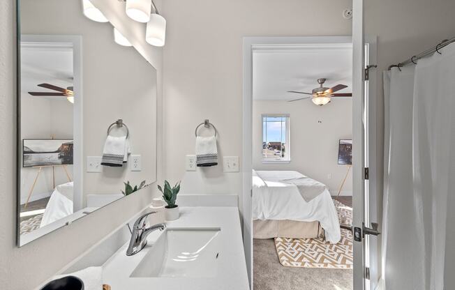 a bathroom with two sinks and a mirror and a room with a bed at The Residences Apartments at Bear Tree | DeForest, WI, DeForest, WI