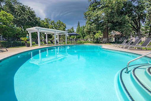 a large swimming pool with chairs and trees in the background