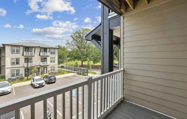 A balcony with a view of a parking lot and apartment building.
