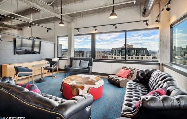 A black leather couch with a red cushion is in the foreground of a bright room with a view of the city at Archer Tower in Denver, CO