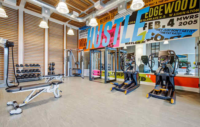 a gym with cardio machines and weights on the floor and a wall with a mural