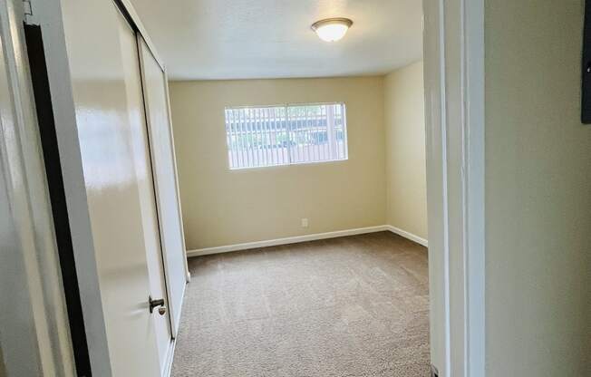 Carpeted bedroom with large window and closet at Plaza Verde Apartments in Escondido, California.