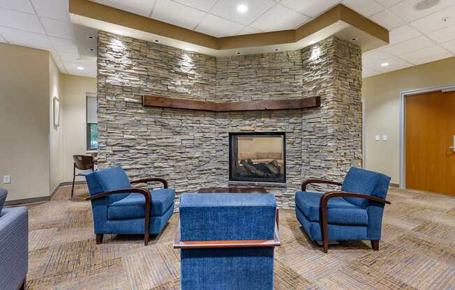 A stone fireplace with a fire going in it and chairs around it.