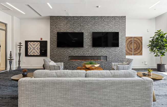 a living room with a gray couch and two televisions on the wall