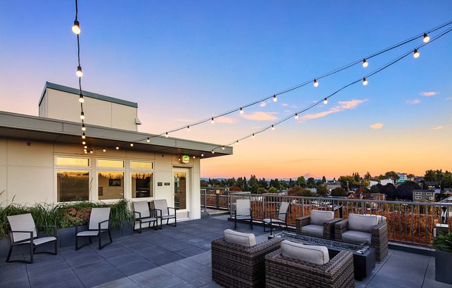 Apartments in Greenwood - The Morrow Rooftop Deck with Comfy Seating, Hanging Lights, Rectangular Fire Feature, and a Panoramic View of the City