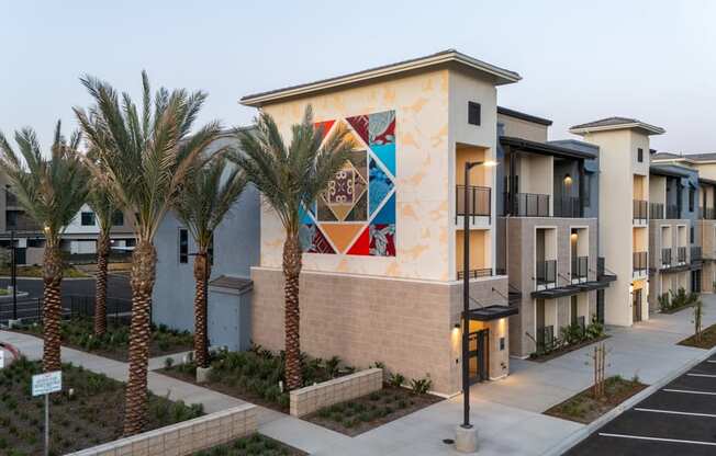 A building with a mural on the side has a row of palm trees in front of it.