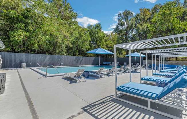 a pool with lounge chairs and umbrellas at The Lorient Apartments, Pensacola