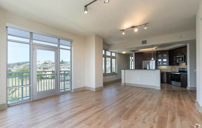 A spacious living room with wooden floors and a kitchen area in the background.