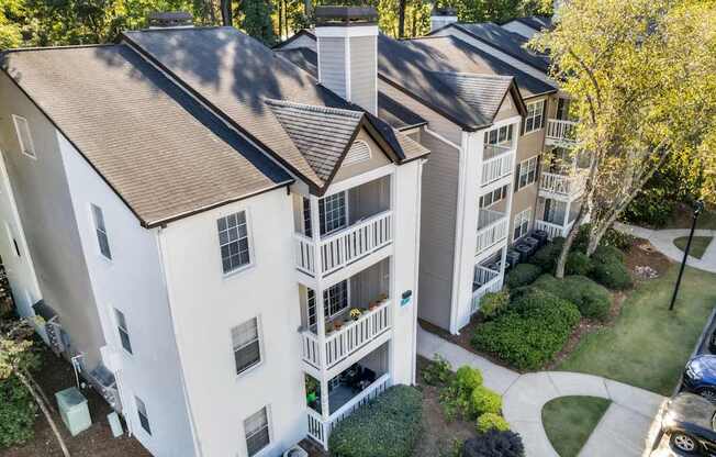 An aerial view of a white apartment building with a brown roof and a parking lot in front.