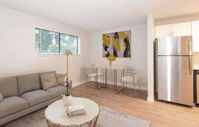 A modern living room with a grey sofa, a white coffee table, and a dining table set up with chairs.