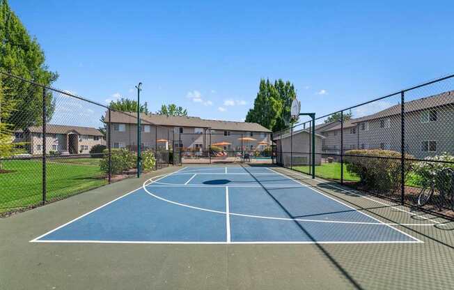 A basketball court is surrounded by a fence and there are buildings in the background.