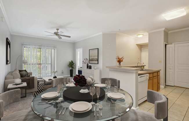 a dining area with a glass table and chairs and a kitchen in the background