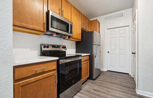 An open-concept apartment with updated lighting, stainless steel appliances, quartz countertops, vinyl plank wood style flooring and wooden cabinets.